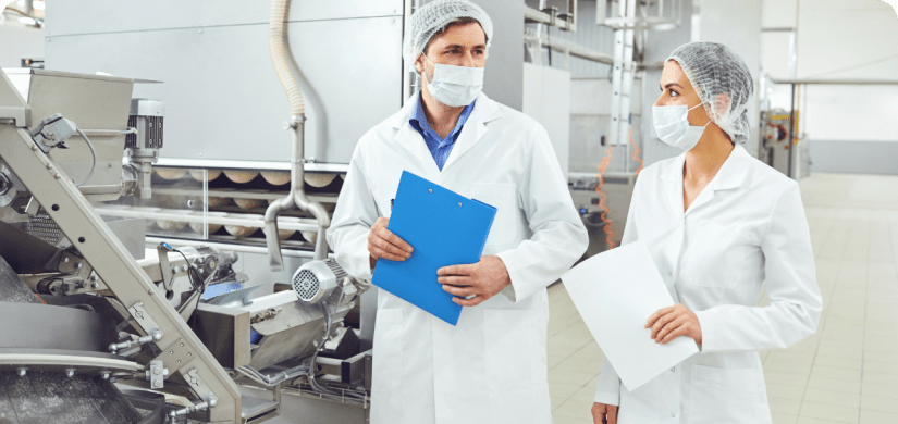 2 food production workers wearing safety outfits documenting facility.