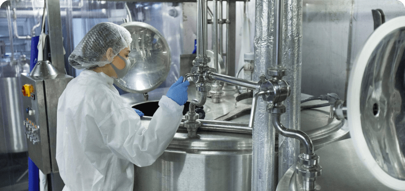 Female worker in food safety clothing looking at stainless steel equipment.